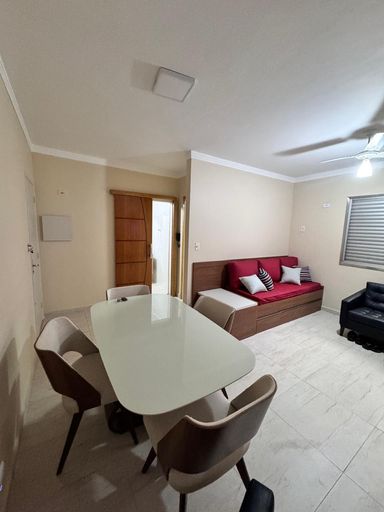 Sala living com ventilador de teto, sofá-cama, poltrona, painel de TV e mesa de jantar.