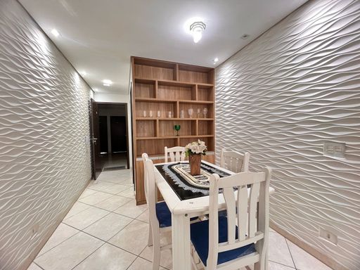 Sala bem iluminada de 2 ambientes com um sofá, painel de TV, teto rebaixado em gesso com iluminação em LED e mesa de jantar.