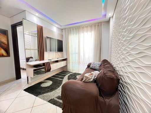 Sala bem iluminada com um sofá, painel de TV, teto rebaixado em gesso com iluminação em LED.