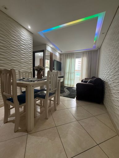 Sala bem iluminada com um sofá, painel de TV, teto rebaixado em gesso com iluminação em LED.