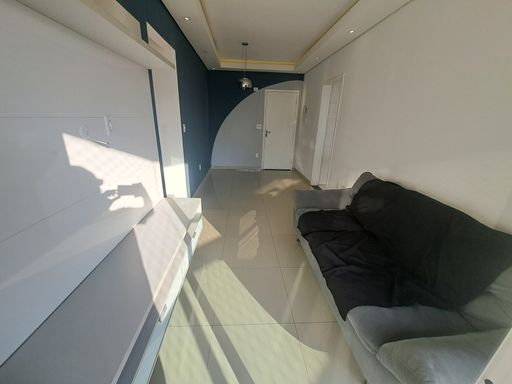 Sala de dois ambientes com muita iluminação natural, uma parede azul e outra branca, com sofá e painel de TV.