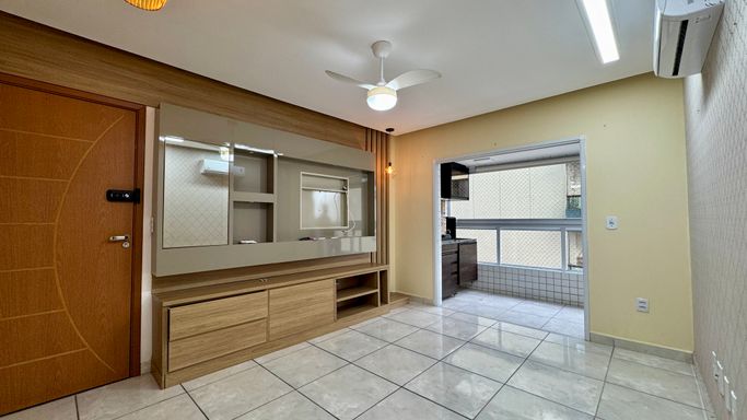 Sala espaçosa e bem iluminada com painel de TV, ventilador de teto e ar-condicionado.