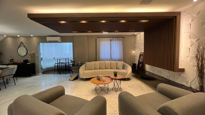 Sala ampla com dois ambientes, sofá, duas poltronas, teto rebaixado com iluminação em LED e sacada envidraçada