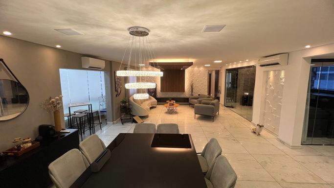 Sala ampla com dois ambientes, equipada com lustre pendente, mesa para oito pessoas, sofá, duas poltronas, ar-condicionado, teto rebaixado com iluminação em LED e sacada envidraçada.
