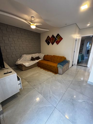Sala ampla de 2 ambientes com dois sofás, ventilador de teto e piso de porcelanato.