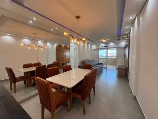 Sala ampla com dois ambientes, teto rebaixado em gesso e iluminação em LED colorido com mesa de jantar de seis lugares, parede espelhada, sofá e painel de TV.