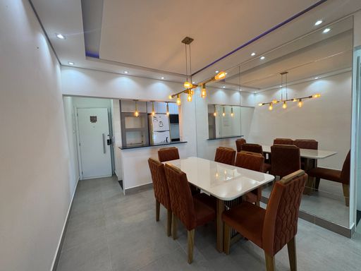 Sala ampla com dois ambientes, teto rebaixado em gesso e iluminação em LED colorido com mesa de jantar de seis lugares, parede espelhada, sofá e painel de TV.
