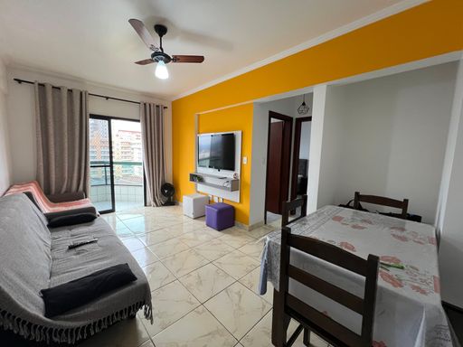Sala ampla e bem iluminada com uma parede amarela, ventilador de teto e sacada.