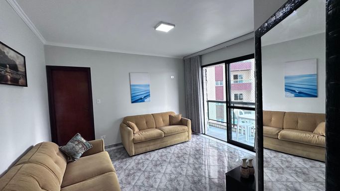 Sala bem iluminada com 2 sofás, espelho e acesso a sacada.