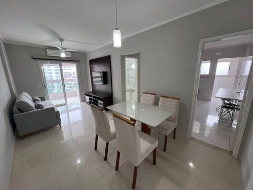 Sala de dois ambientes com mesa de jantar para quatro pessoas, sofá, painel de TV, ar-condicionado e acesso à sacada gourmet.