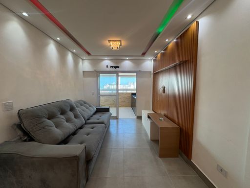 Sala ampla com dois ambientes, teto rebaixado em gesso e iluminação em LED colorido com mesa de jantar de seis lugares, parede espelhada, sofá e painel de TV.