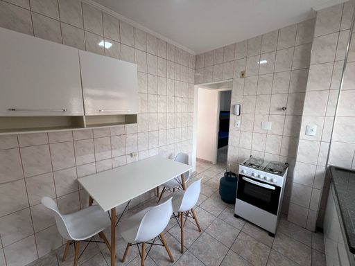 Cozinha com pia, gabinete, fogão e mesa branca de 04 lugares.