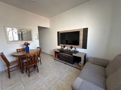 Sala bem iluminada com dois sofás, mesa de jantar, rack, TV e ventilador de teto.