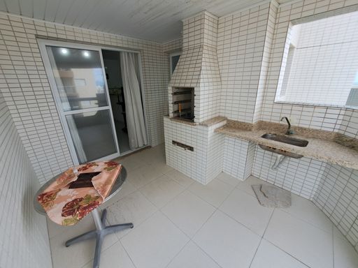 Sacada gourmet com churrasqueira a carvão e vista lateral para o mar.