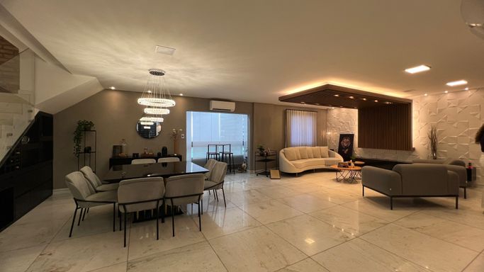 Sala ampla com dois ambientes, equipada com lustre pendente, mesa para oito pessoas, sofá, duas poltronas, ar-condicionado, teto rebaixado com iluminação em LED e sacada envidraçada.