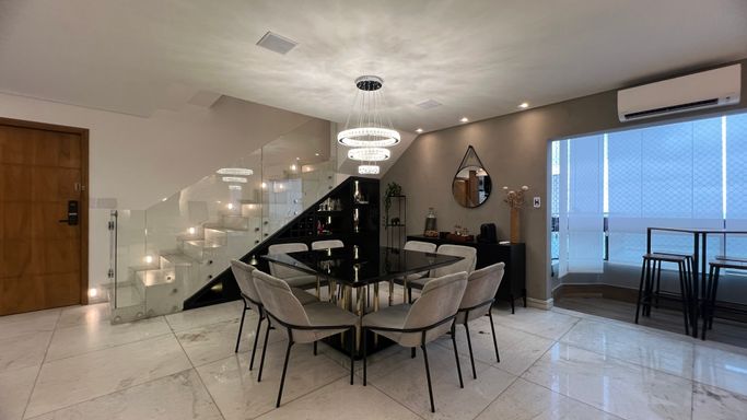 Sala ampla com dois ambientes, lustre pendente, mesa de oito lugares e ar-condicionado.