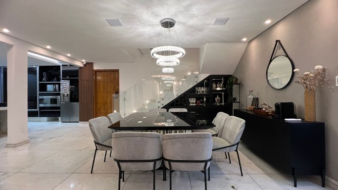 Sala ampla com dois ambientes, lustre pendente, mesa de oito lugares e ar-condicionado.