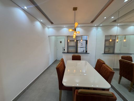 Sala ampla com dois ambientes, teto rebaixado em gesso e iluminação em LED colorido com mesa de jantar de seis lugares, parede espelhada, sofá e painel de TV.