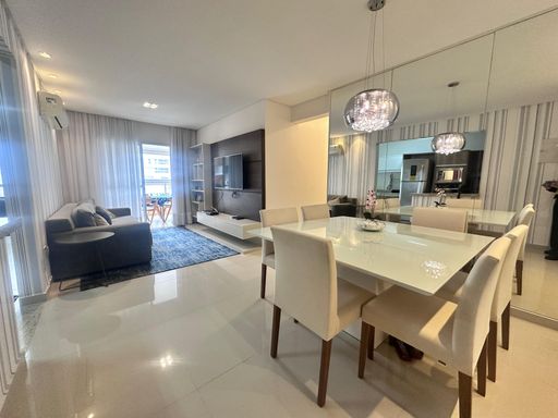 Sala ampla com dois ambientes, com ar-condicionado, sofá, mesa de jantar, parede espelhada e um elegante lustre pendente.