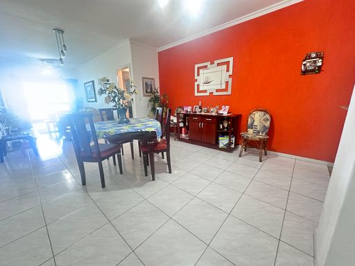 Sala bem iluminada de dois ambientes com uma parede laranja, mesa de jantar e ventilador de teto.
