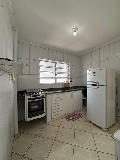 Cozinha com janela, pia preta com gabinete branco e geladeira branca e fogão emmbutido de 4 bocas.