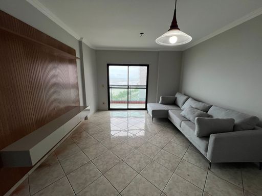 Sala de dois ambientes com painel de TV, sofá cinza com sacada com vista para o mar.