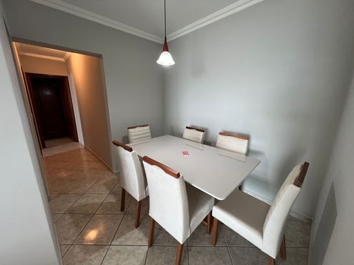 Sala de dois ambientes com sofá cinza, painel de TV e mesa de jantar para seis pessoas.