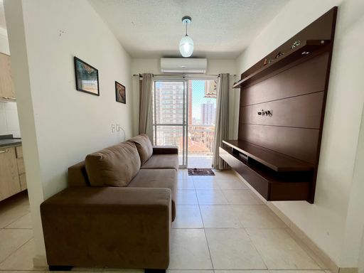 Sala bem iluminada com um sofá, painel de TV, ar-condicionado e acesso a sacada.