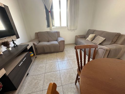 Sala bem iluminada com dois sofás, mesa de jantar, rack, TV e ventilador de teto.