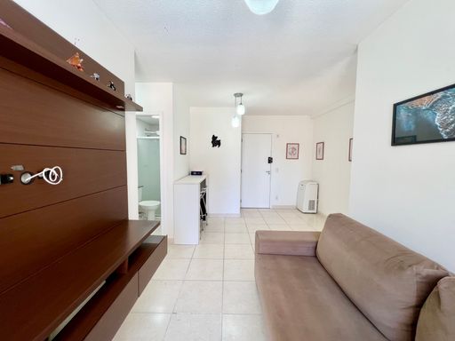 Sala bem iluminada com um sofá, painel de TV, ar-condicionado e acesso a sacada.