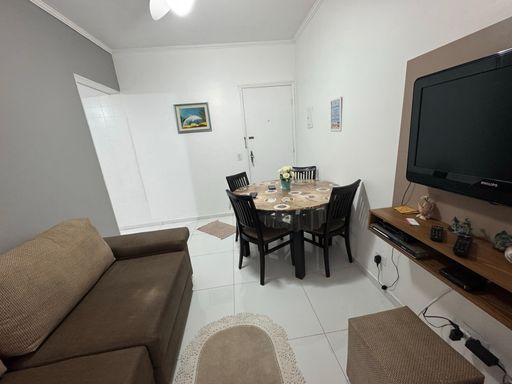 Sala mobiliada com sofá, mesa de jantar e painel de TV.