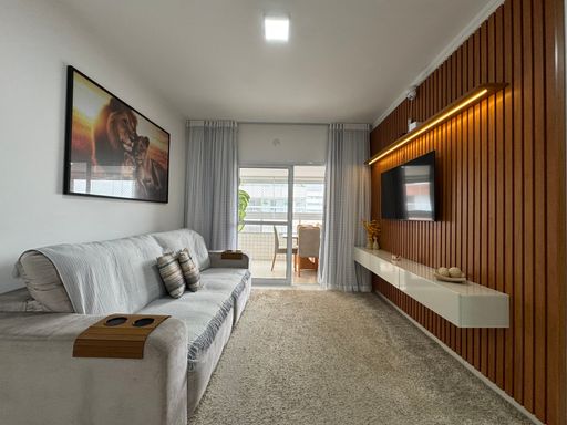 Sala ampla com painel de TV, com acesso a sacada gourmet.