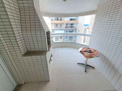 Sacada gourmet com churrasqueira a carvão e vista lateral para o mar.