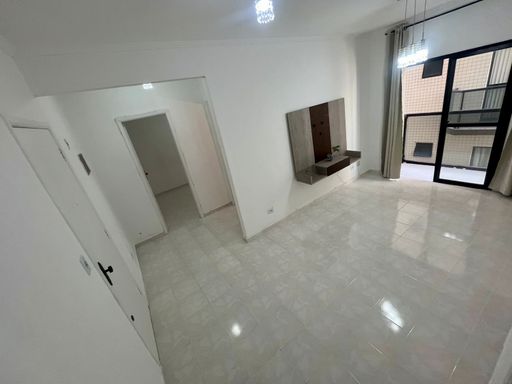 Sala espaçosa com paredes brancas, painel de TV e uma sacada.