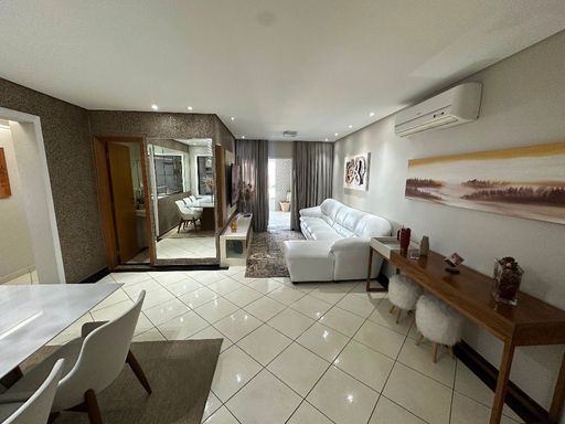 Sala ampla com dois ambientes, parede espelhada, ar-condicionado, sofá branco e mesa de jantar para seis pessoas.