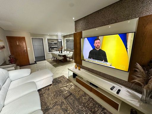 Sala com dois ambientes, sofá branco e acesso à sacada gourmet.