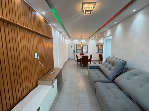Sala ampla com dois ambientes, teto rebaixado em gesso e iluminação em LED colorido com mesa de jantar de seis lugares, parede espelhada, sofá e painel de TV.