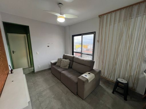 Sala bem iluminada com um sofá cinza, painel de TV e uma sacada.