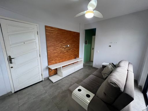 Sala bem iluminada com um sofá cinza, painel de TV e uma sacada.