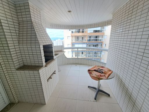 Sacada gourmet com churrasqueira a carvão e vista lateral para o mar.