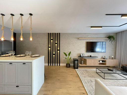 Sala espaçosa, muito bem iluminada, com sofá e piso laminado, integrada a uma cozinha americana totalmente planejada.