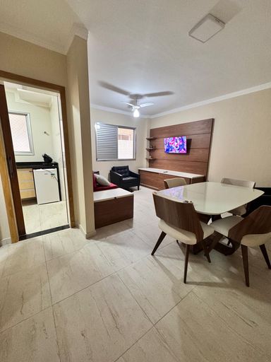 Sala living com ventilador de teto, sofá-cama, poltrona, painel de TV e mesa de jantar.