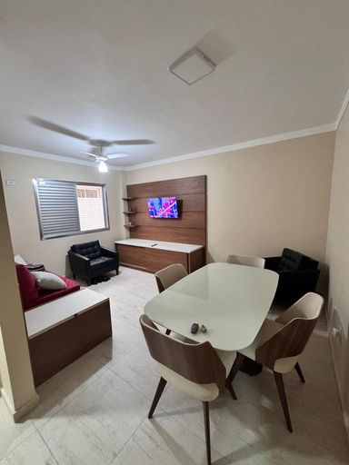 Sala living com ventilador de teto, sofá-cama, poltrona, painel de TV e mesa de jantar.