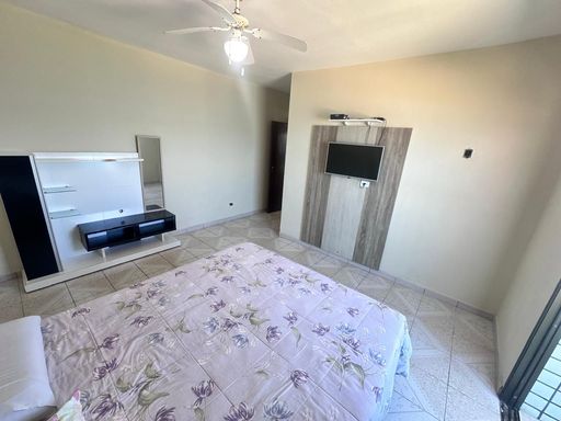 Suíte ampla com muita iluminação natural, ventilador de teto e sacada envidraçada com vista para o mar.