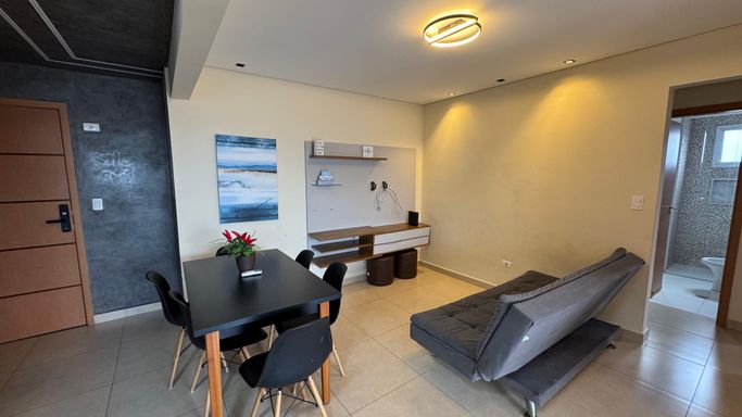 Sala de 2 ambientes com uma mesa de jantar, sofá cama e painel de TV.