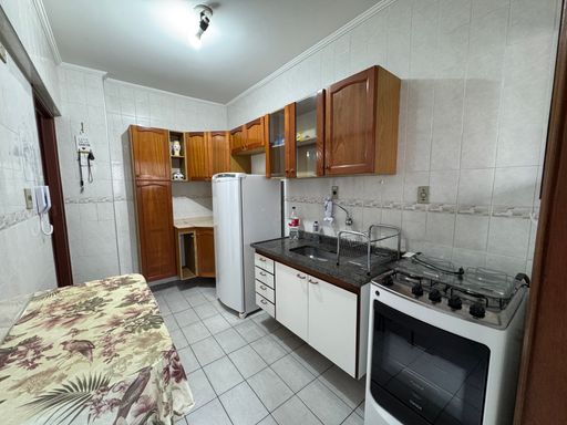 Cozinha com armários, geladeira, pia, fogão e mesa.