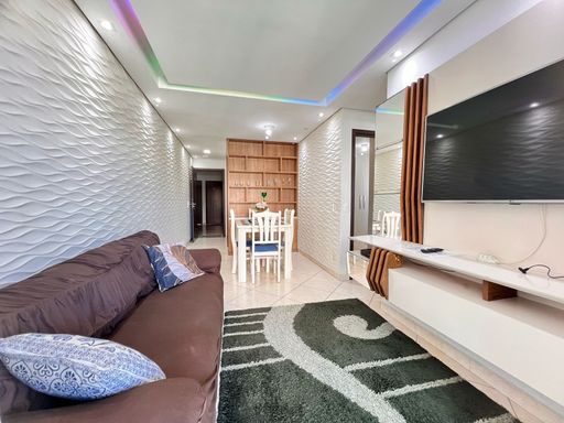 Sala bem iluminada de 2 ambientes com um sofá, painel de TV, teto rebaixado em gesso com iluminação em LED.