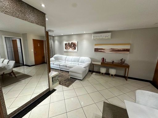 Sala ampla com dois ambientes, parede espelhada, sofá branco e mesa de jantar para seis pessoas.