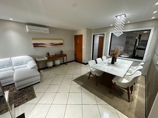 Sala ampla com dois ambientes, parede espelhada, sofá branco e mesa de jantar para seis pessoas