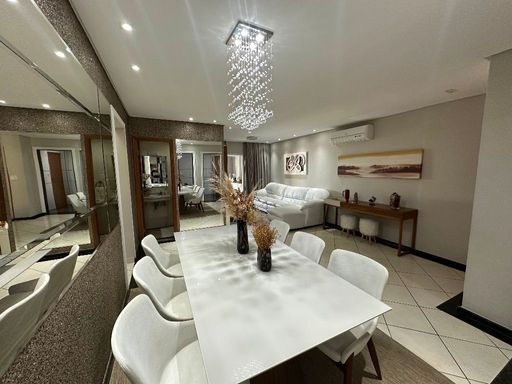 Sala ampla com dois ambientes, parede espelhada, ar-condicionado, sofá branco e mesa de jantar para seis pessoas.